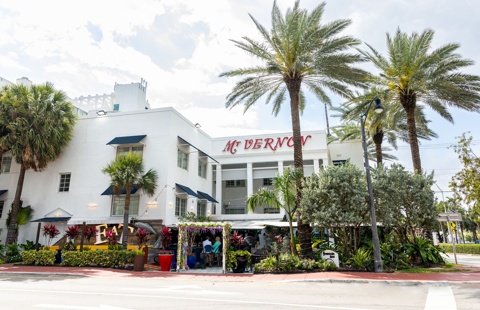 The image shows a white building named "McAlpin," surrounded by palm trees and greenery, with outdoor seating and people visible.