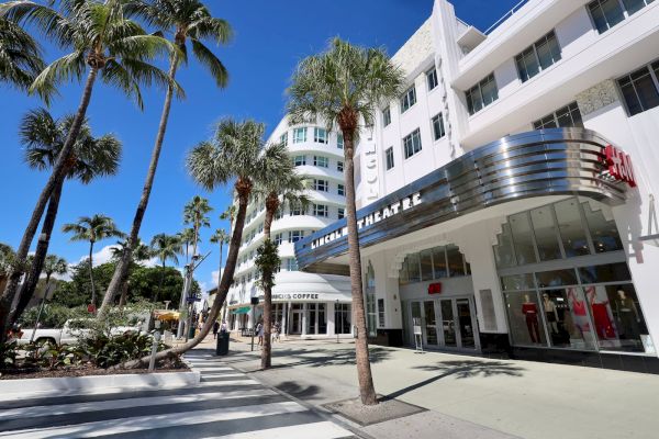 The image shows a street scene with palm trees, a white building labeled "Lincold Theatre," and a storefront with mannequins.